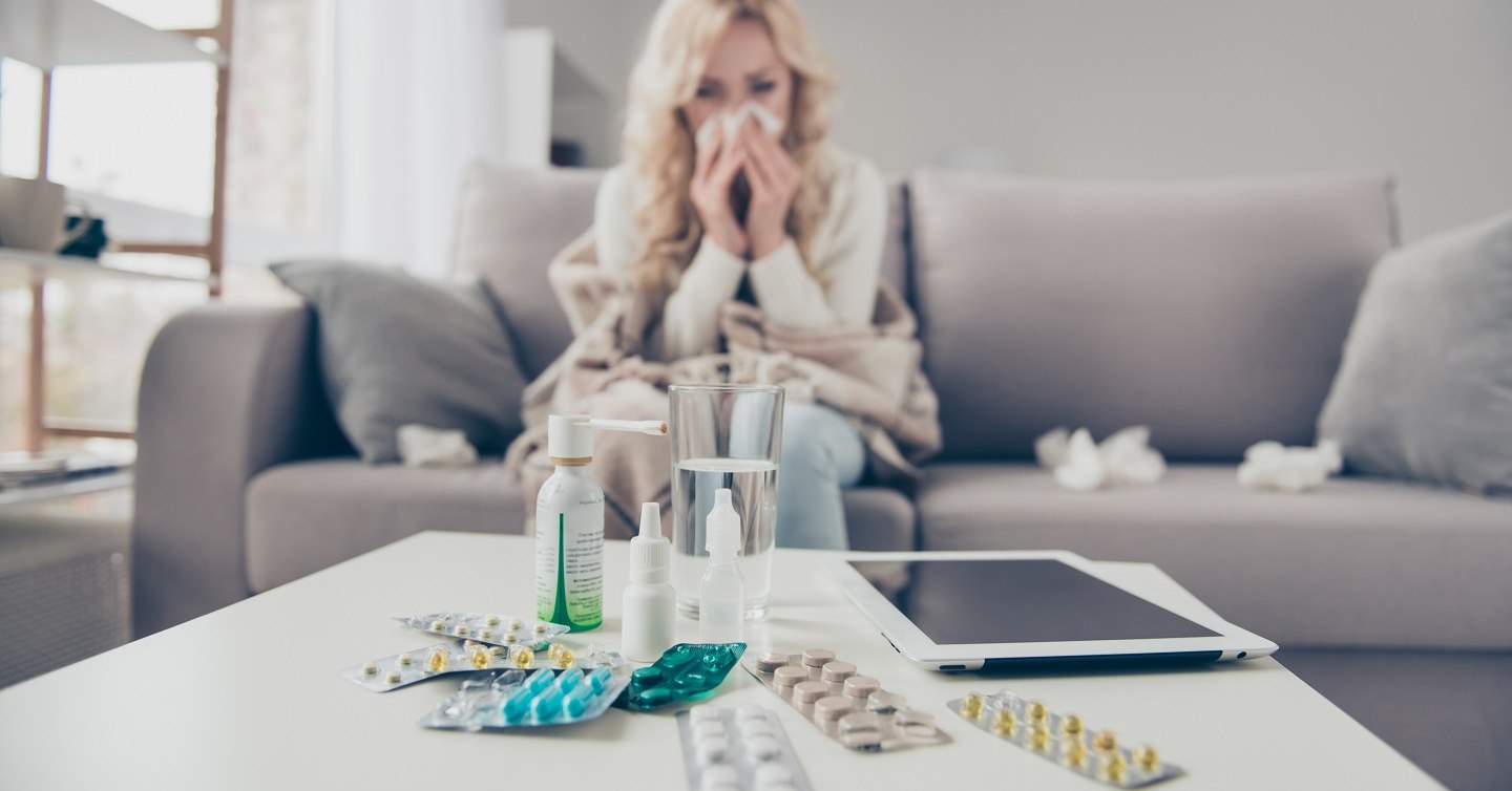 person sniffling with kleenex and allergy medication on table in front of them