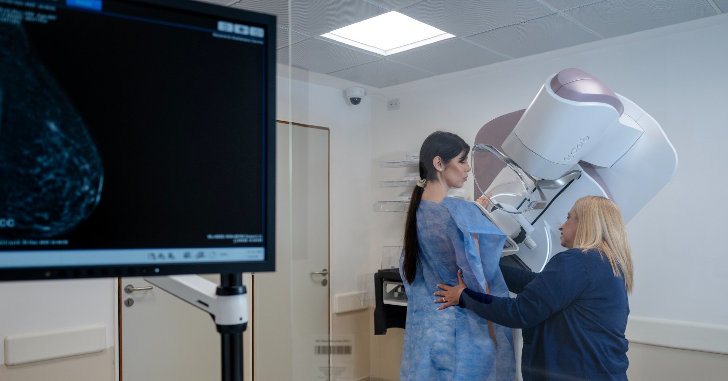 a woman being guided toward a 3d mammogram machine by a mammogram tech